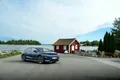 Volkswagen ID.7 vor einem roten Holzhaus am Wasser